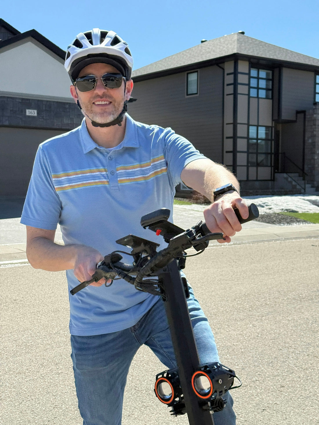 Smiling man in helmet and sunglasses holds an electric scooter